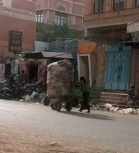 الصرخة في صورة| زوجة إعلامي يمني مرموق تدفع عربة نفايات في صنعاء لسد جوع أطفالها 